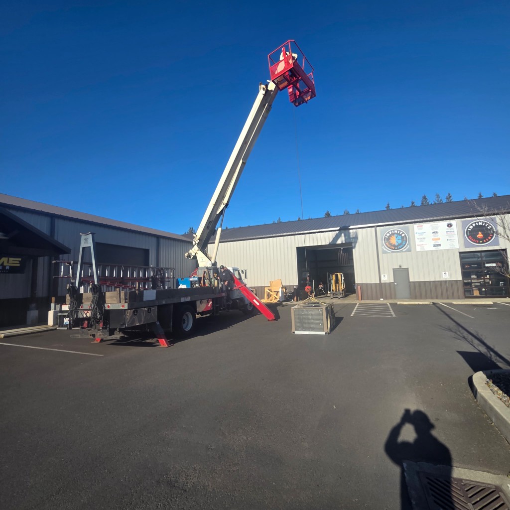 Truck-mounted boom lift handling HVAC equipment at a commercial site